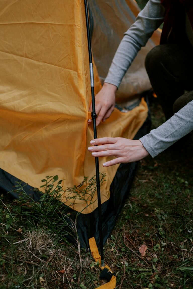 Close-up of a person setting up a tent, focusing on hands and tent pole assembly.